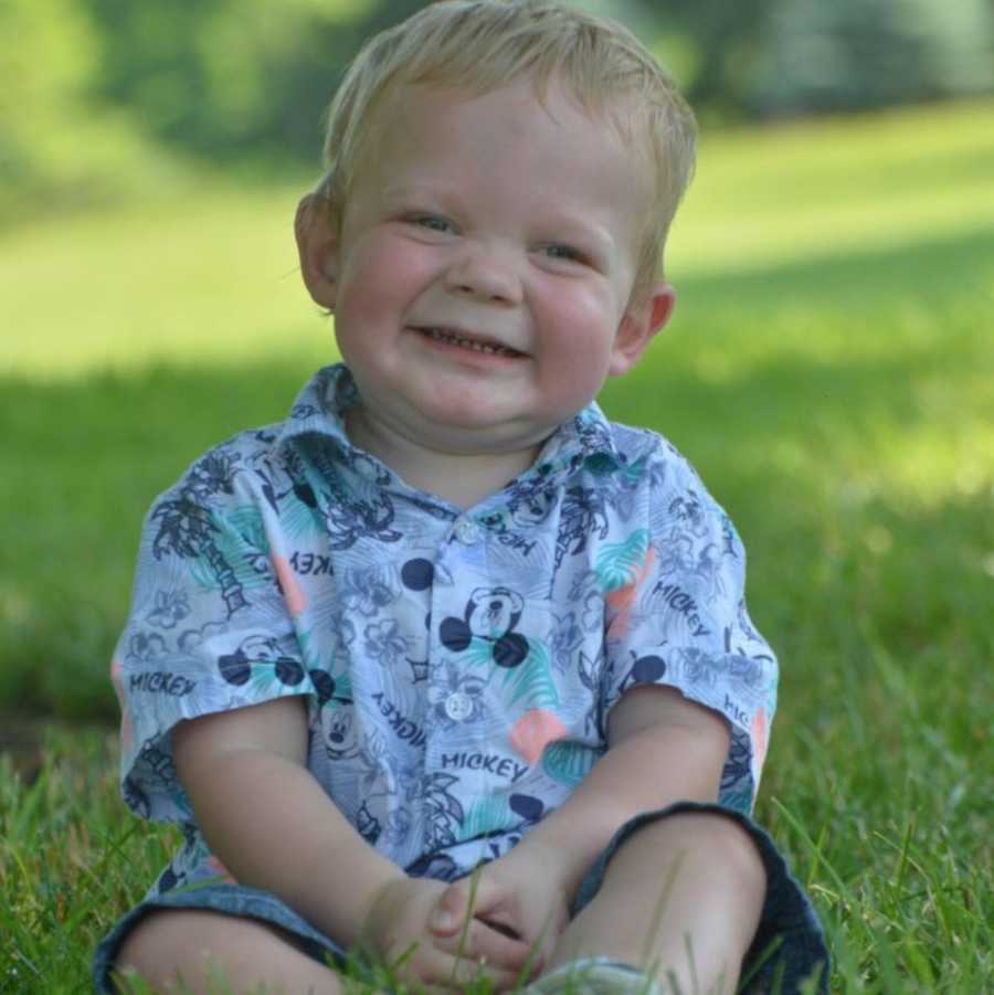 Little boy who battled cancer sits on ground outside smiling