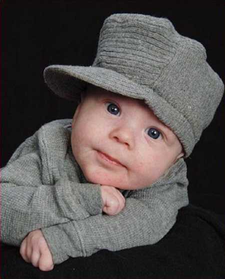 Baby boy in gray shirt and hat poses for photoshoot
