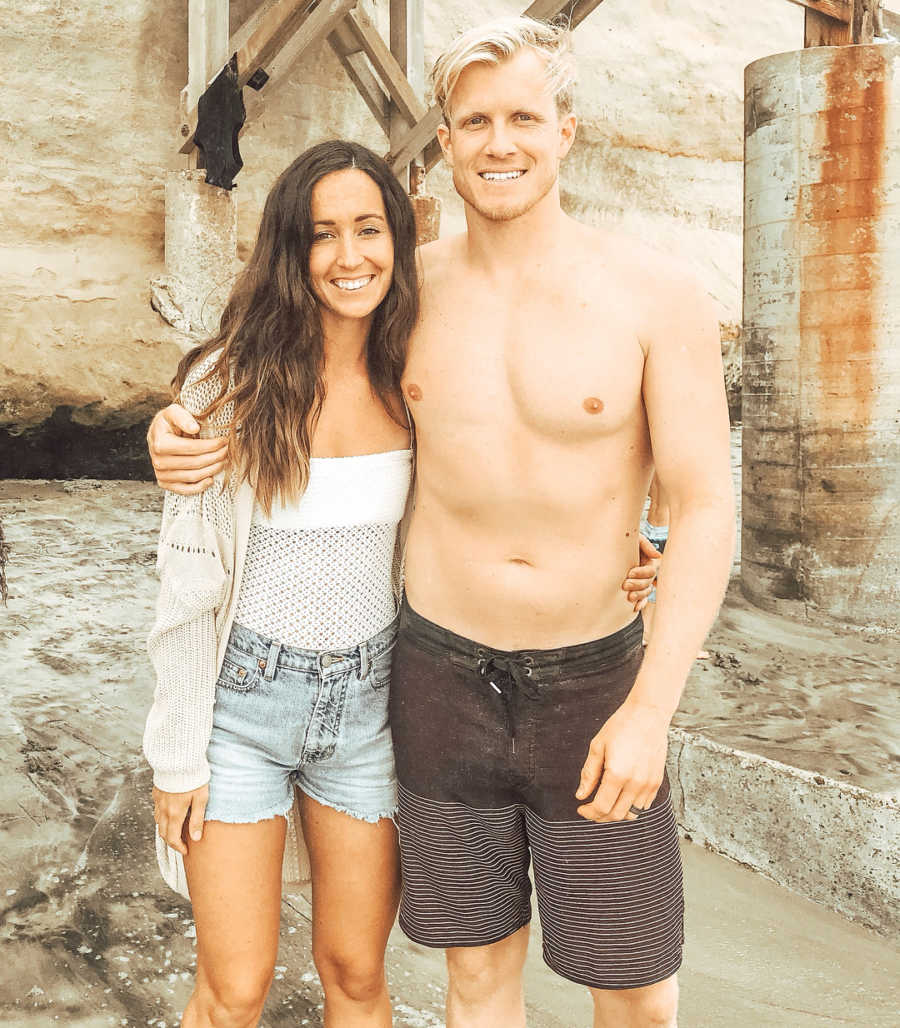 Husband and wife stand arm in arm smiling outside