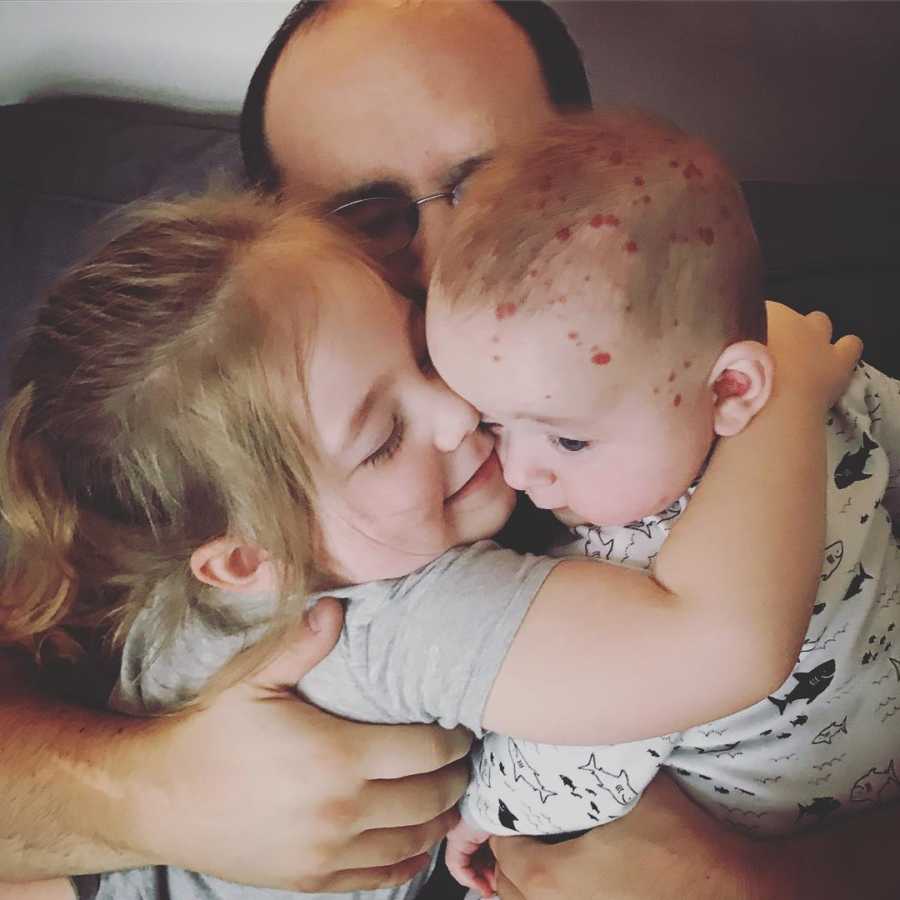 Father sits with arms wrapped around his two children that sit on his lap