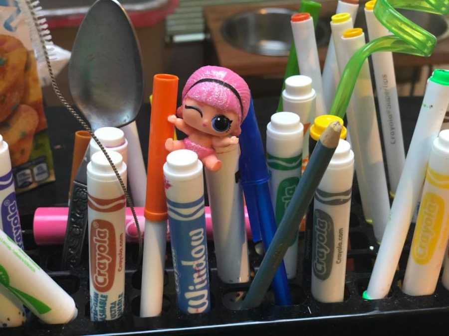 Markers standing up in container with tiny toy sits on markers