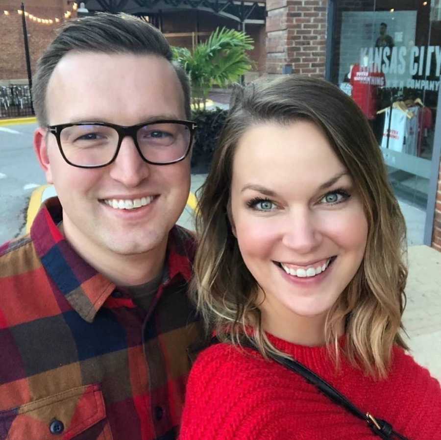 Husband and wife smile in selfie as they walk on sidewalk