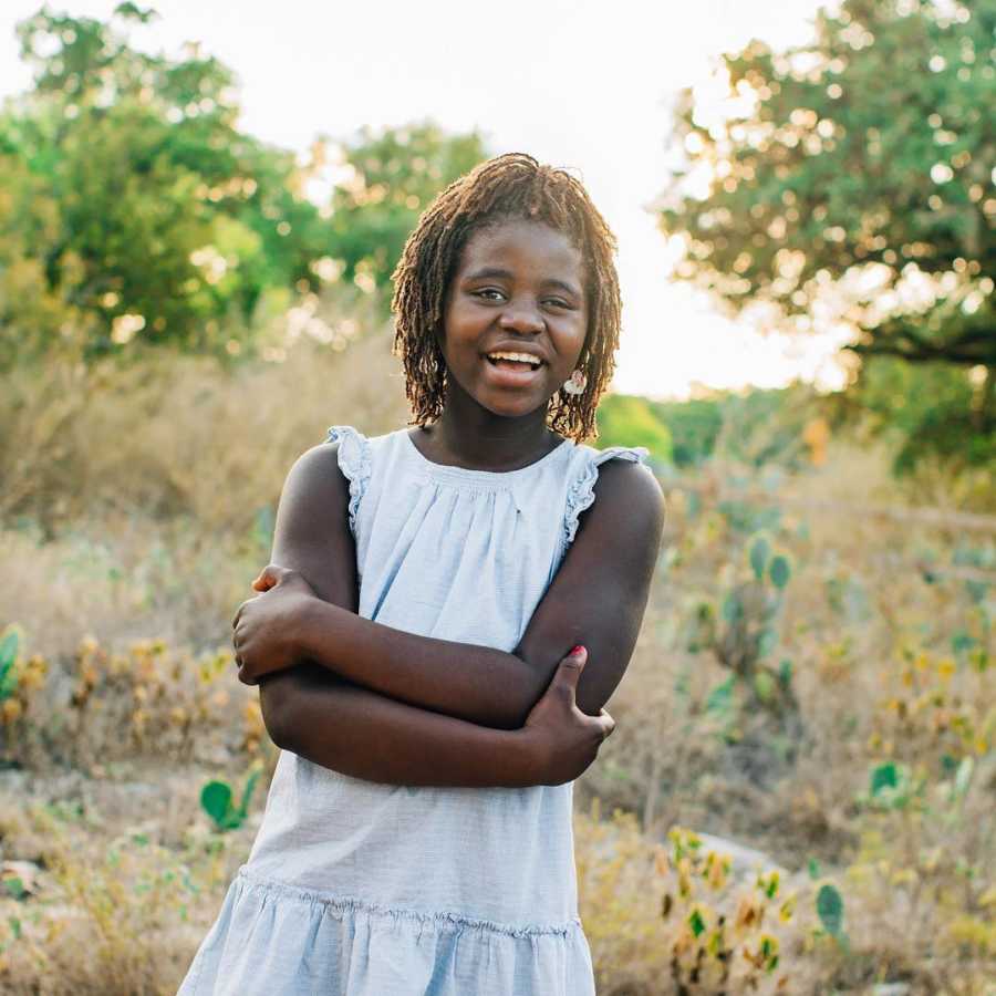 Adopted teen stands in field smiling holding her arms