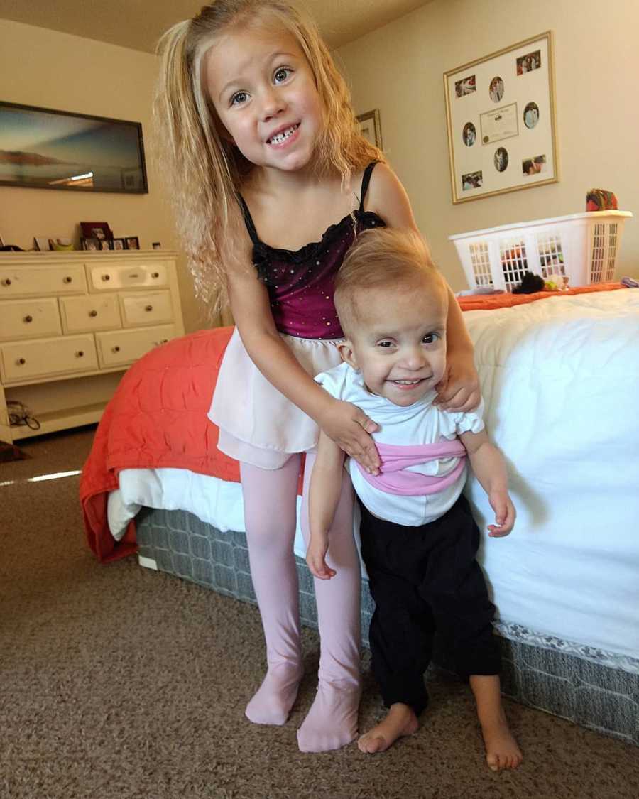 Baby with unknown disease stands in bedroom with older sister
