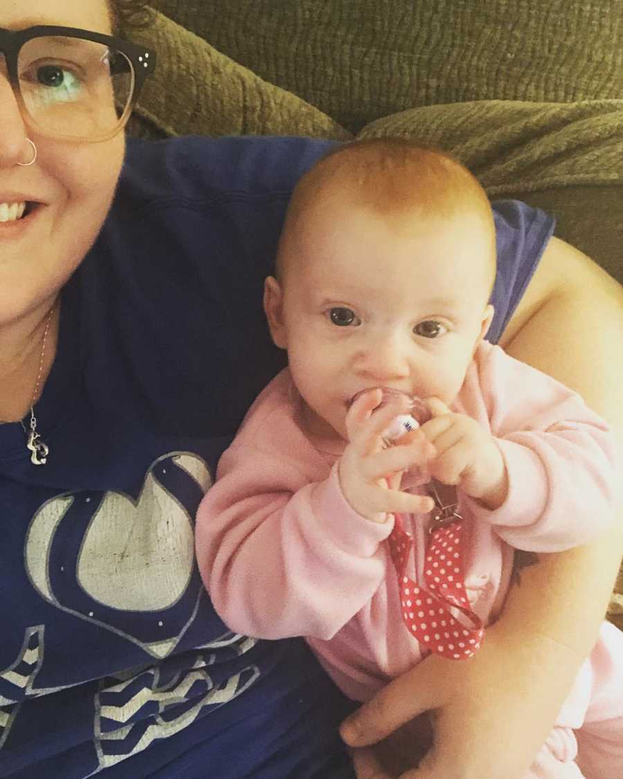 Mother smiles in selfie with baby girl who lays in her arm