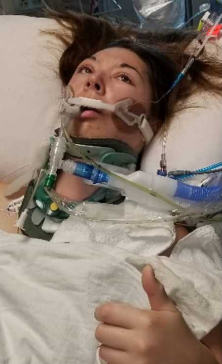 Young woman with Ehlers-Danlos Syndrome lays in hospital bed with thumbs up