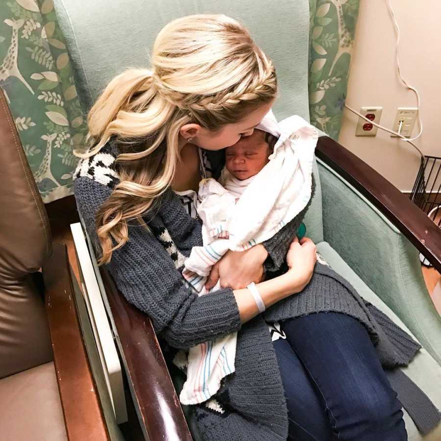 Woman sits in chair of hospital room holding her adopted newborn