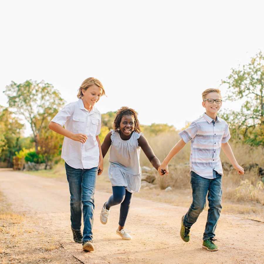 Two brother walk on dirt path holding hands with their adopted sister