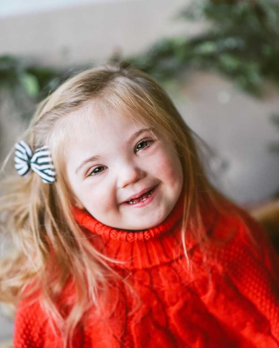 Little girl with down syndrome smiles in red turtleneck sweater
