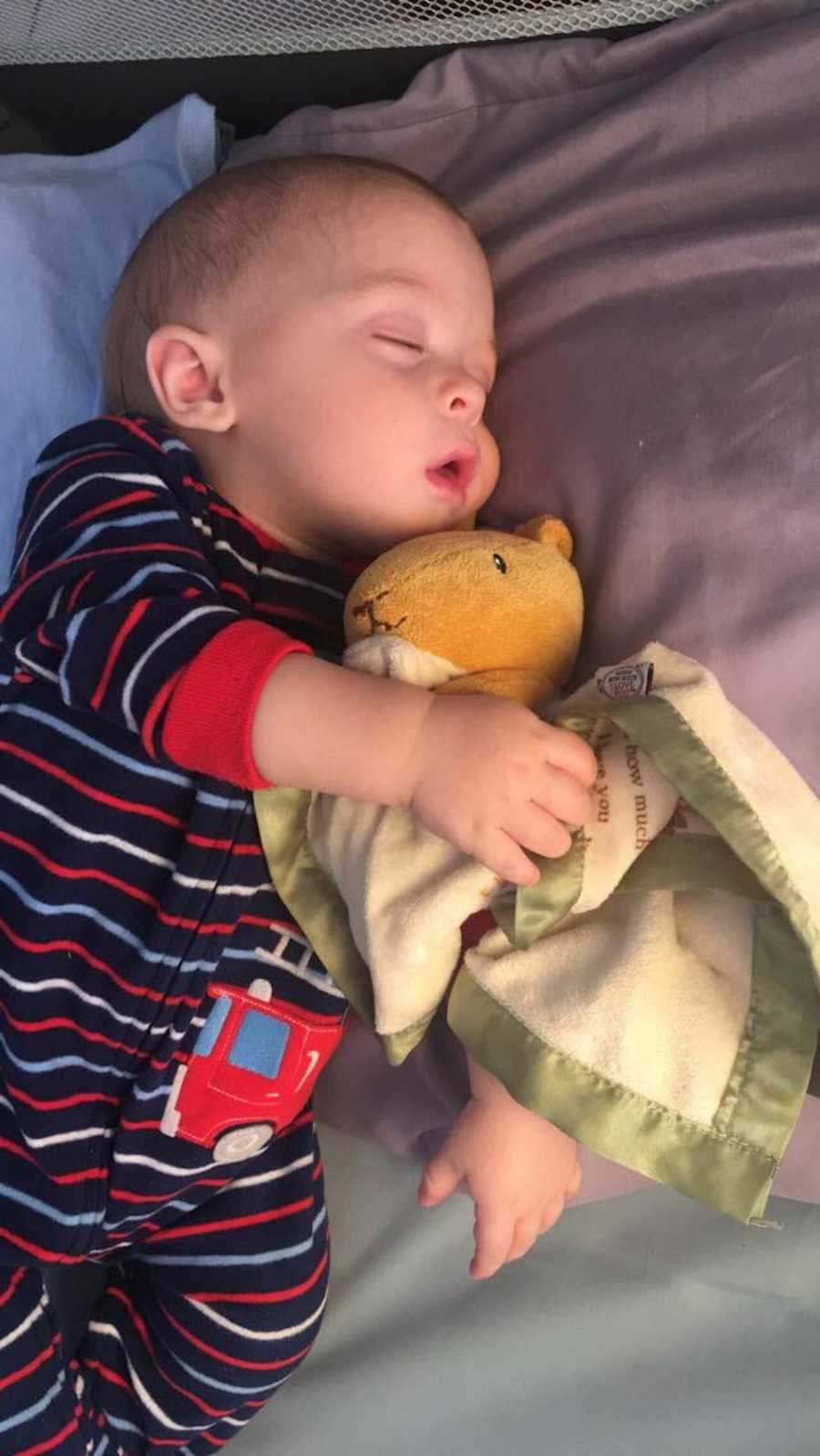 Baby boy lays in bed asleep holding on to blanket