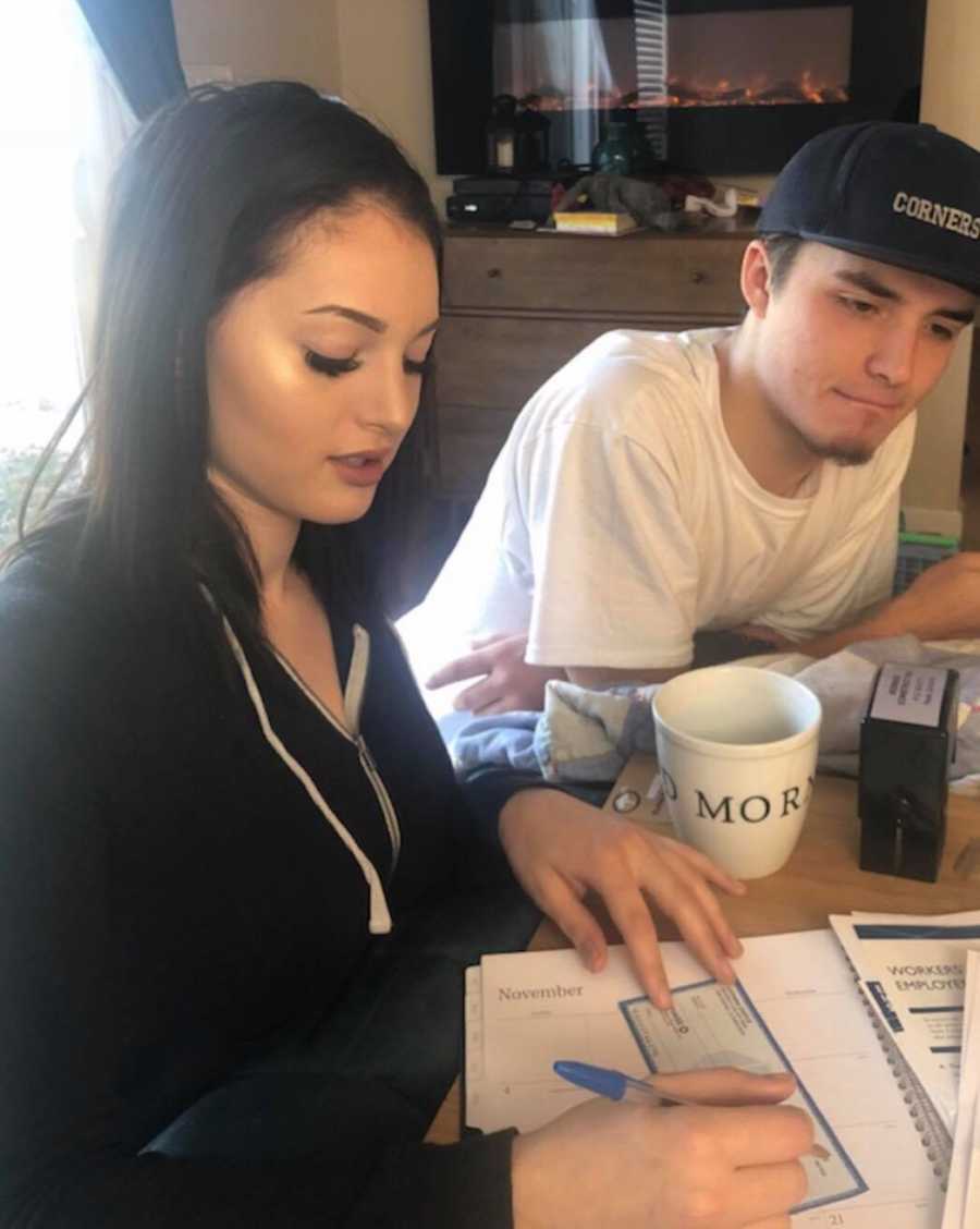 Young woman sits at table writing check beside her boyfriend