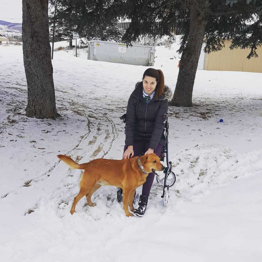 Young woman with Ehlers-Danlos Syndrome sits in wheelchair outside in snowy weather with dog