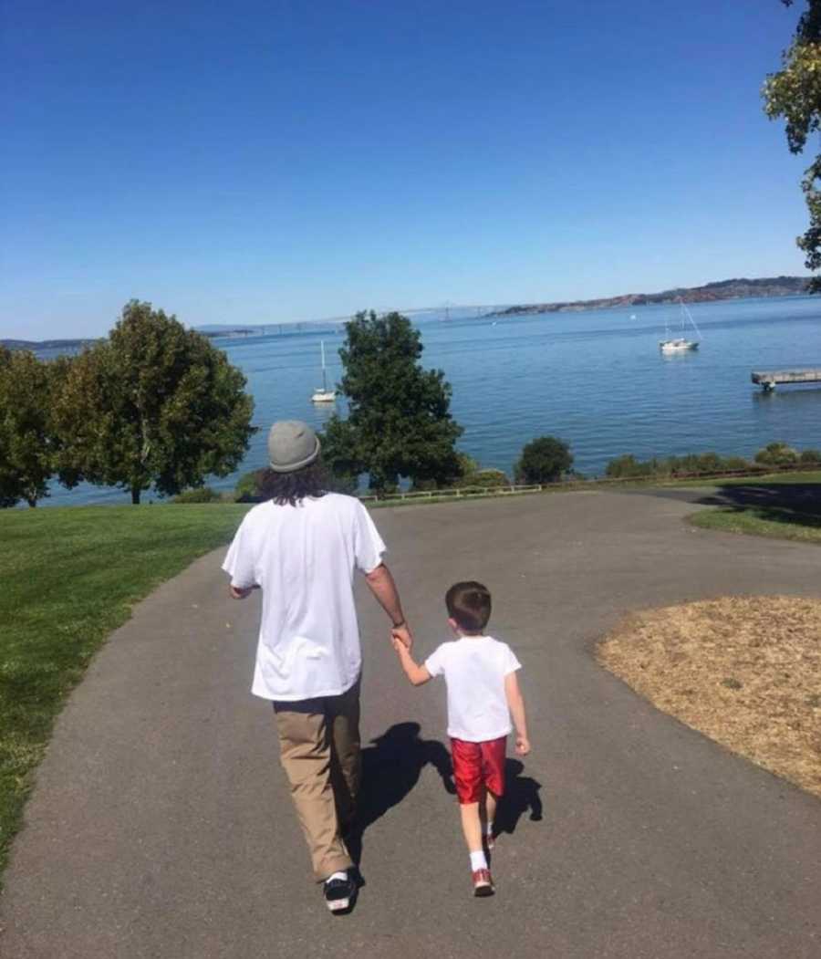 Young man who has since passed from drug overdose walks on path holding hand with younger brother