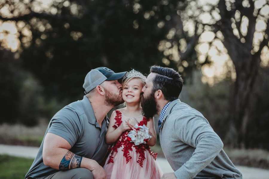 Dad's crouch down beside daughter as they kiss her on her cheeks