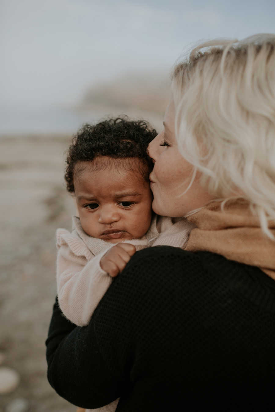 Mother holds and kisses adopted baby girl on side of head