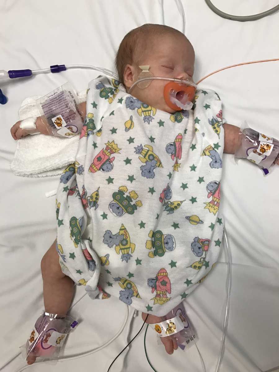 Newborn baby with pacifier in mouth lays on back in NICU