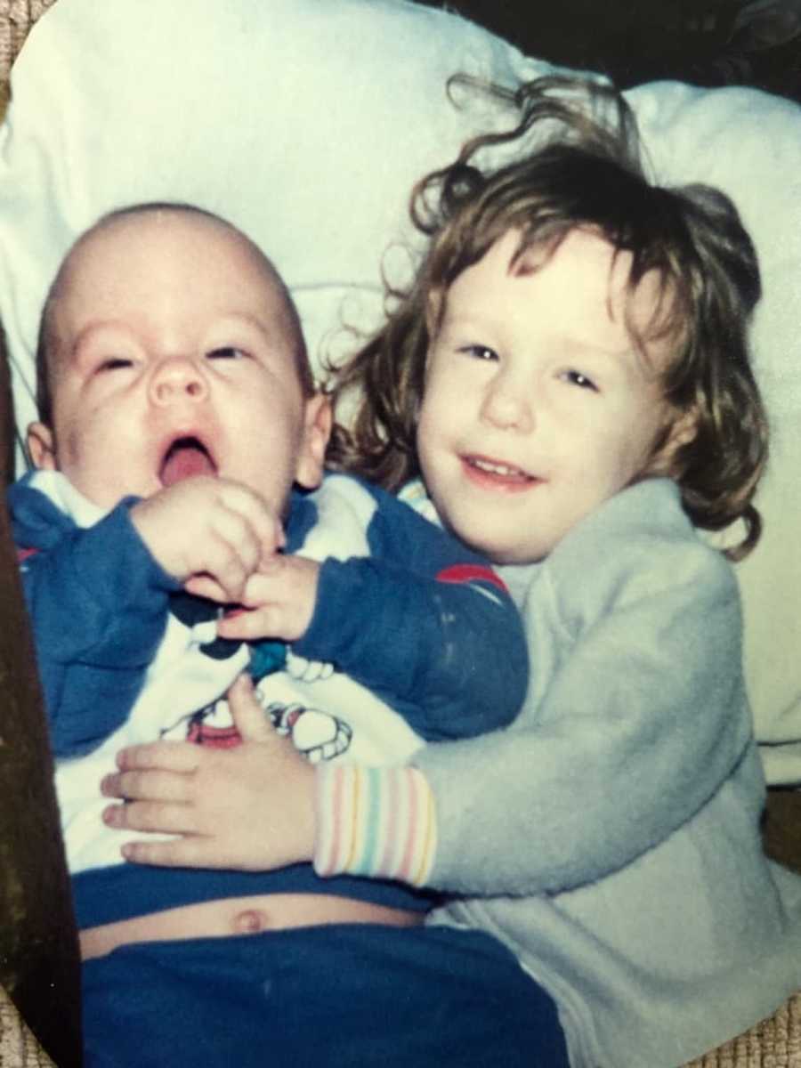 Little girl lays with arms around her baby brother