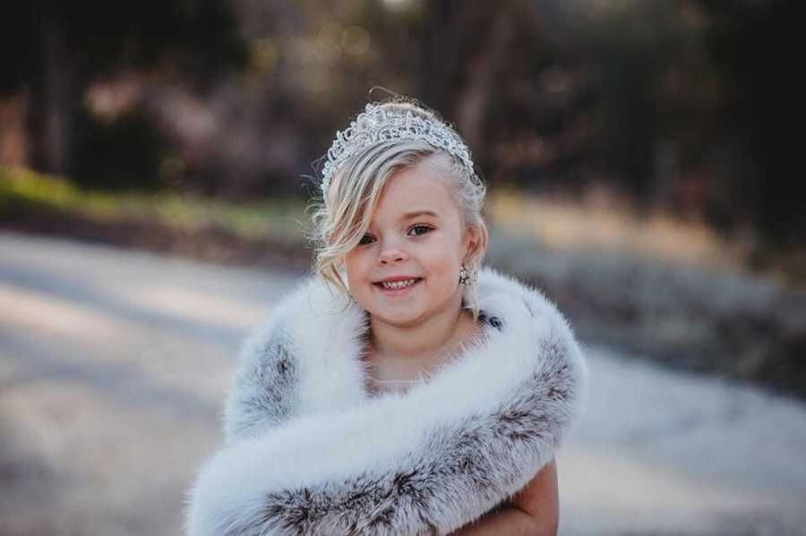 Young girl with two dads stands outside wearing crown and fur scarf