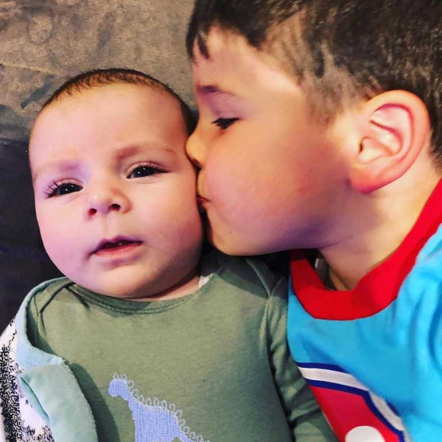 Little boy kisses cheek of baby brother