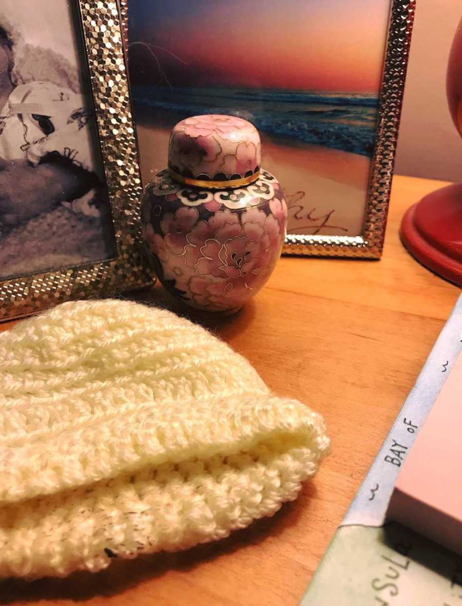 White baby hat and small urn sit on table for baby who passed away