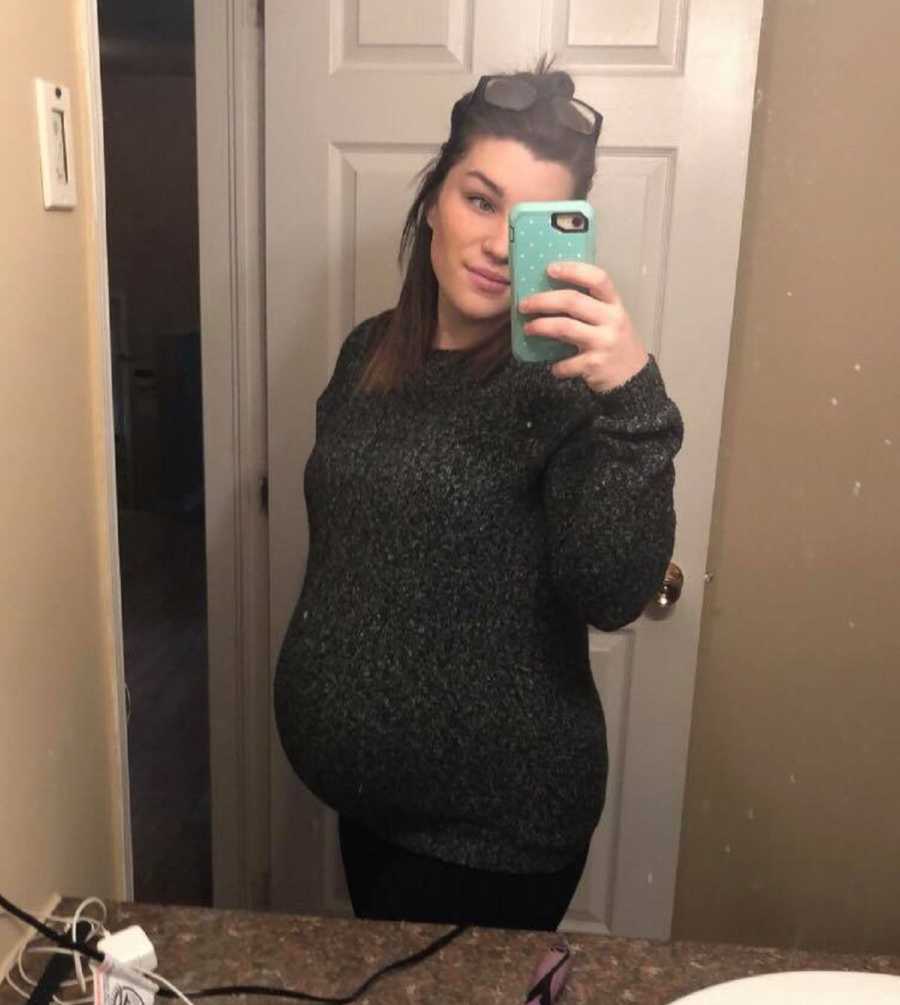 Pregnant woman smiles in mirror selfie in home bathroom