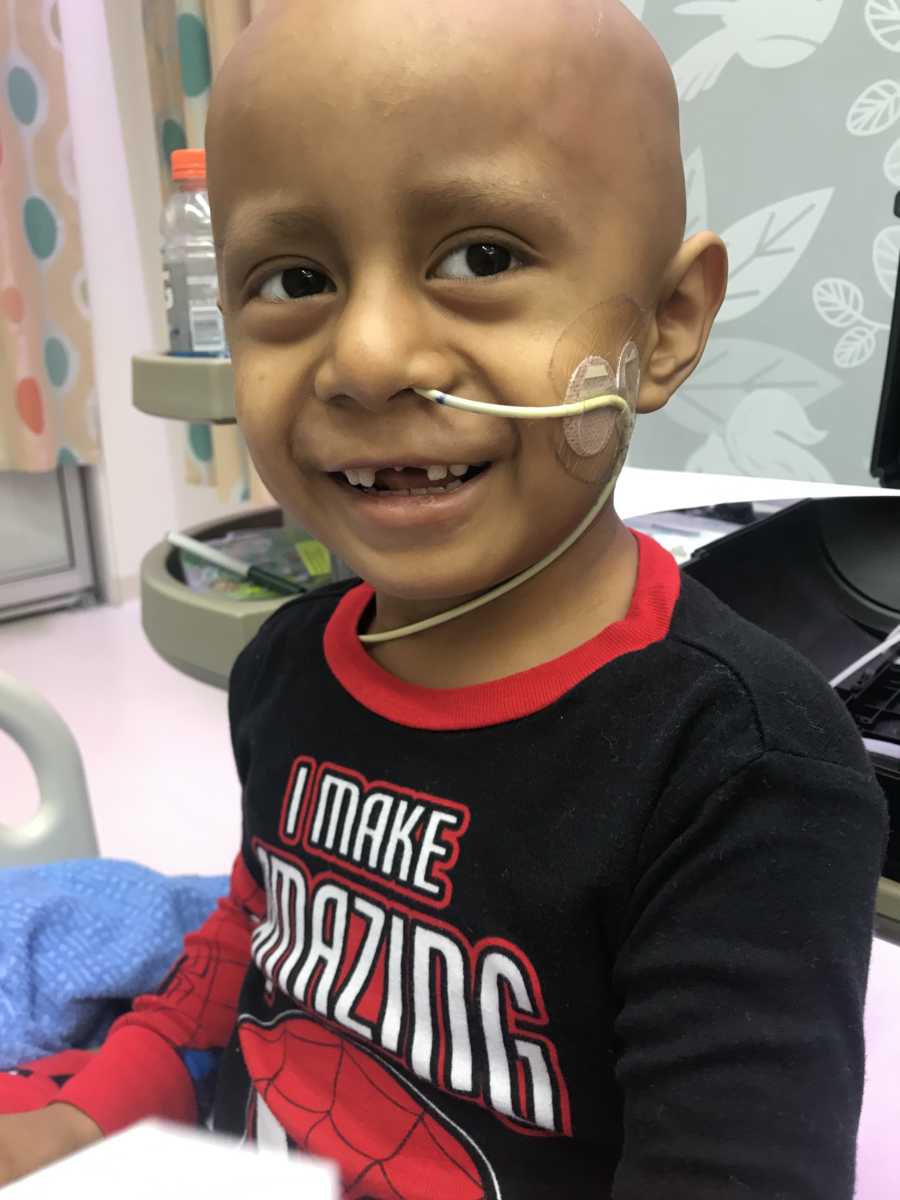 Little boy with cancer sits smiling in hospital room with tube up his nose