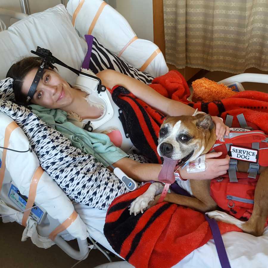 Young woman with Ehlers-Danlos Syndrome lays in hospital bed in full body brace and dog in her bed