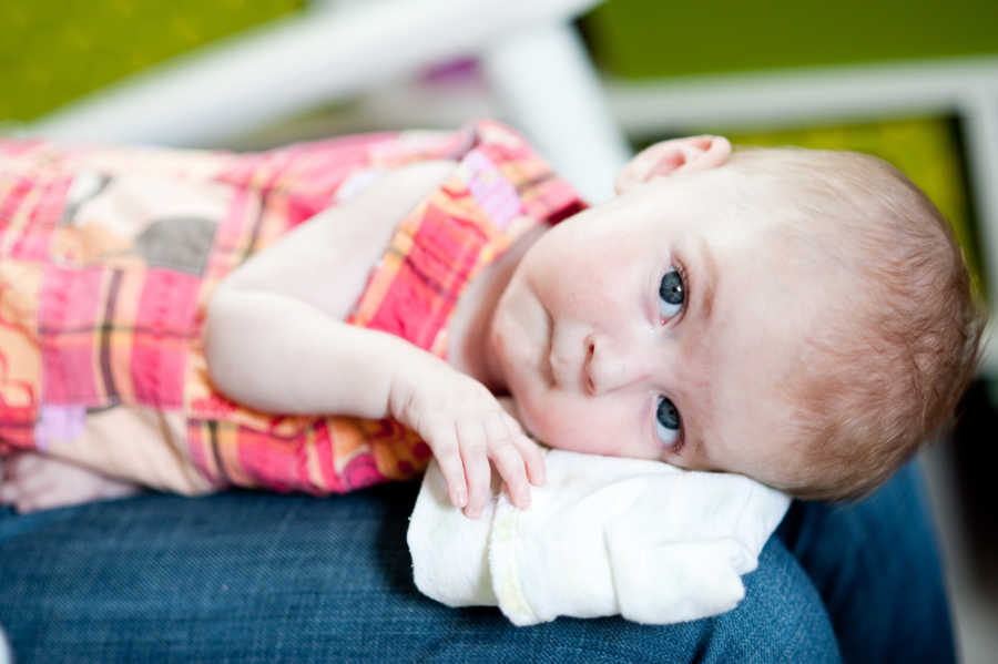 Baby girl with Spinal Muscular Atrophy lays on parent's legs