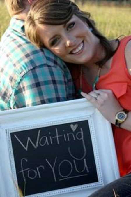 Woman leans on husband's shoulder holding sign that says, "Waiting for you"