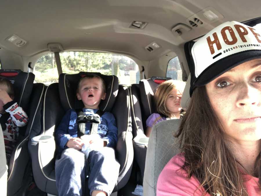 Mother takes selfie in car with three kids in back seat in car seats