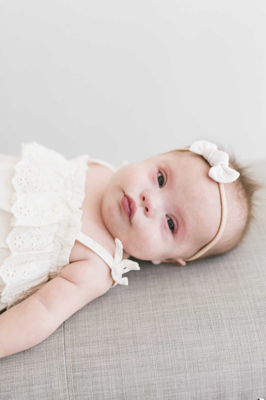 Newborn with down syndrome lay son back wearing white bow and dress