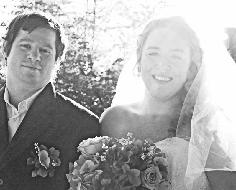 Bride and groom stand arm in arm outside smiling