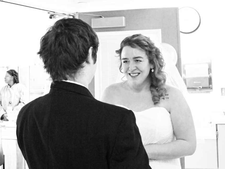 Bride smiles at groom as they stand in hospital room
