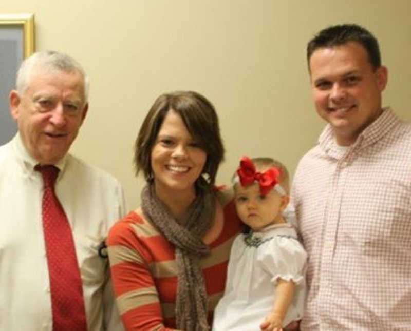 Husband and wife smile beside man and their adopted little girl
