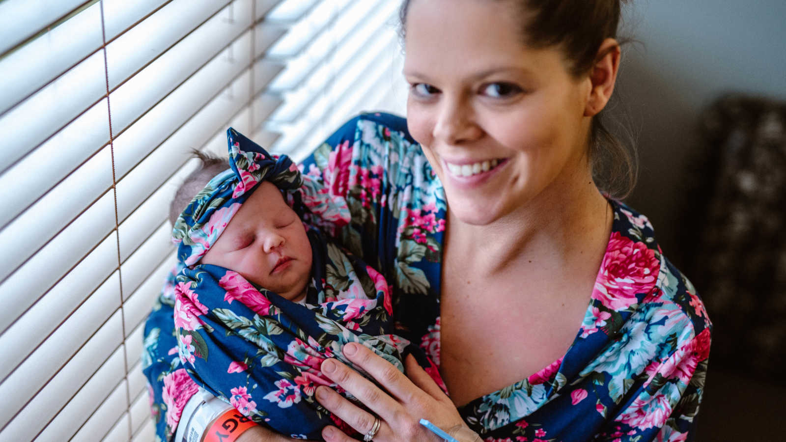 Mother smiles in holding newborn baby wrapped in blanket that matches mother's robe