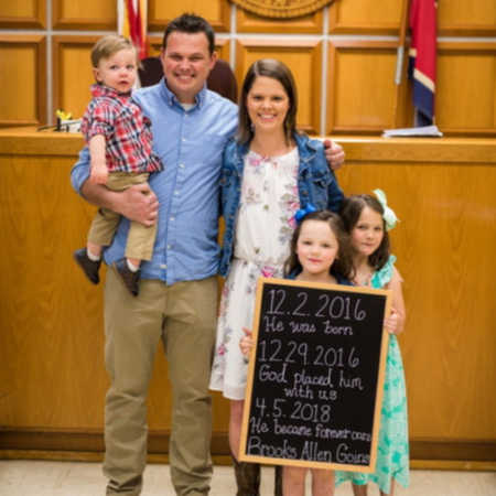 Husband and wife stand in adoption court with their two adopted children and biological daughter