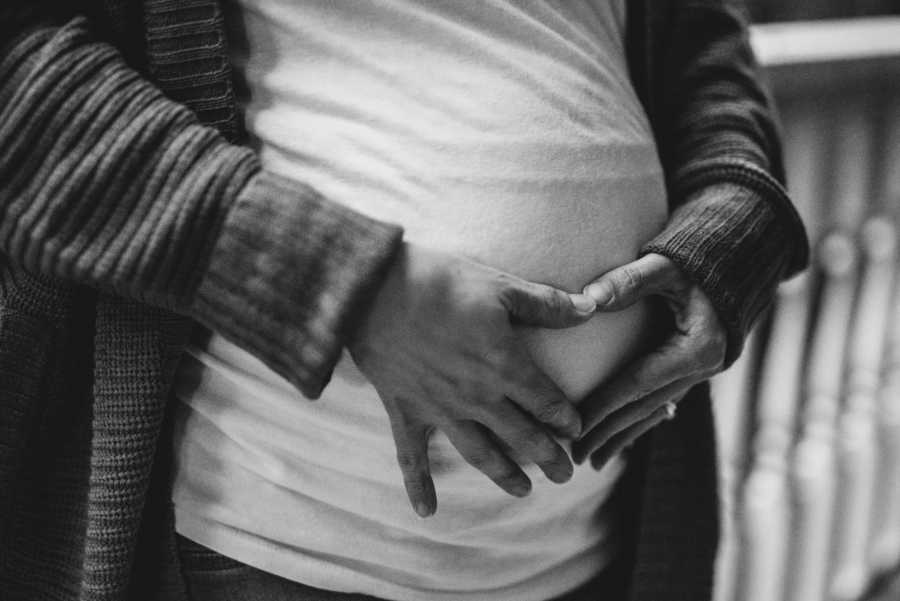 Womans hands are placed on her pregnant stomach in shape of heart