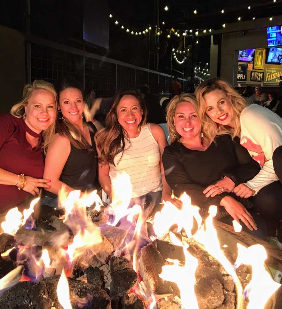 Five woman sits smiling beside fire pit