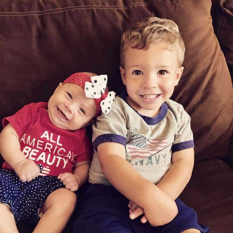 Little boy sits on couch beside baby sister