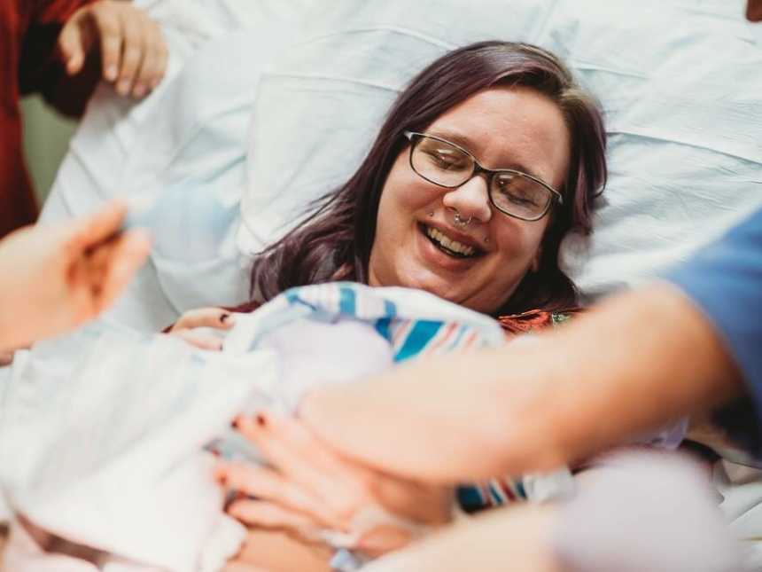 Woman smiles in hospital bed as she looks at newborn wrapped in blanket