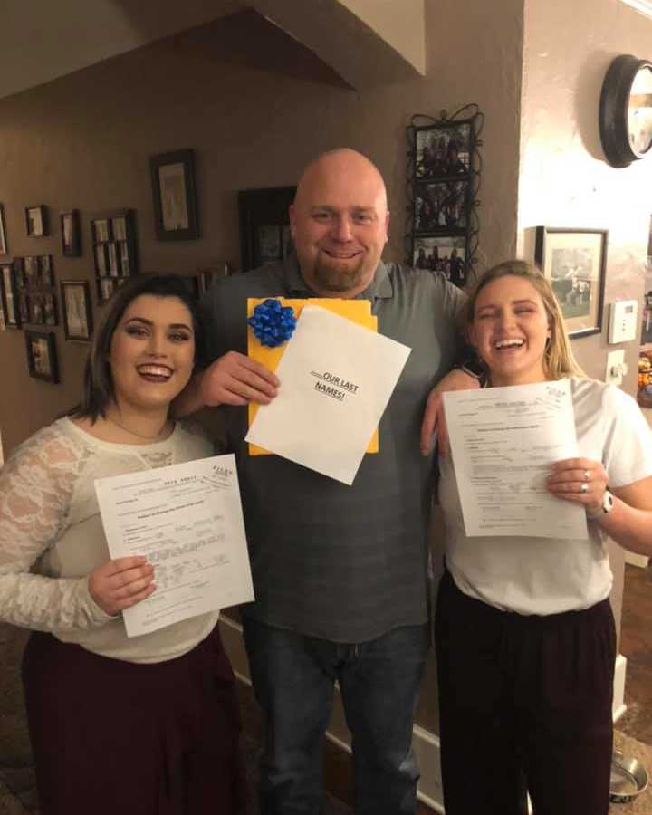 Man stands holding papers beside his adopted daughters who hold adoption papers