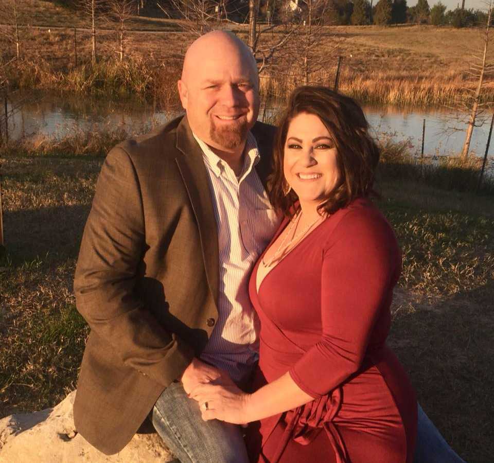 Man sits outside on rock as wife stands beside him