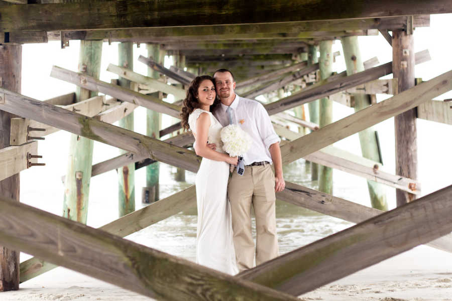 Bride and groom stand smiling under pier