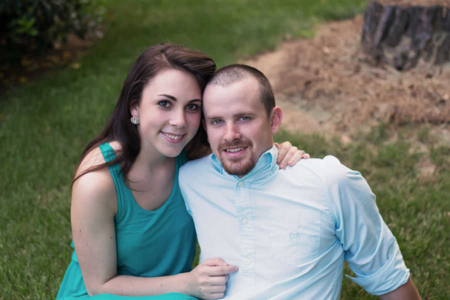 Husband and wife sit outside on ground smiling