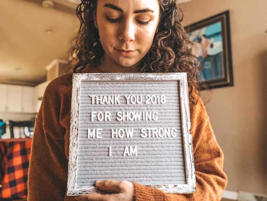 Woman who miscarried holds sign saying, "Thank you 2018 for showing me how strong I am"