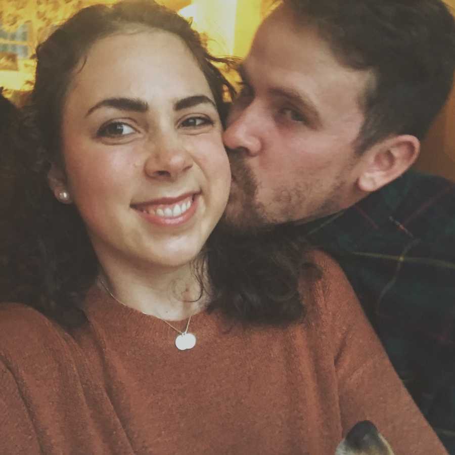 Wife smiles in selfie as husband kisses her cheek