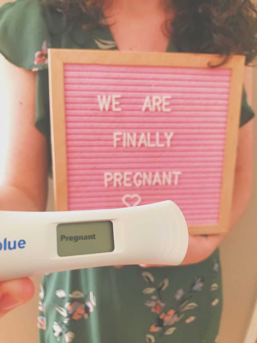 Woman holds sign saying, "we are finally pregnant" and positive pregnancy test in front of it