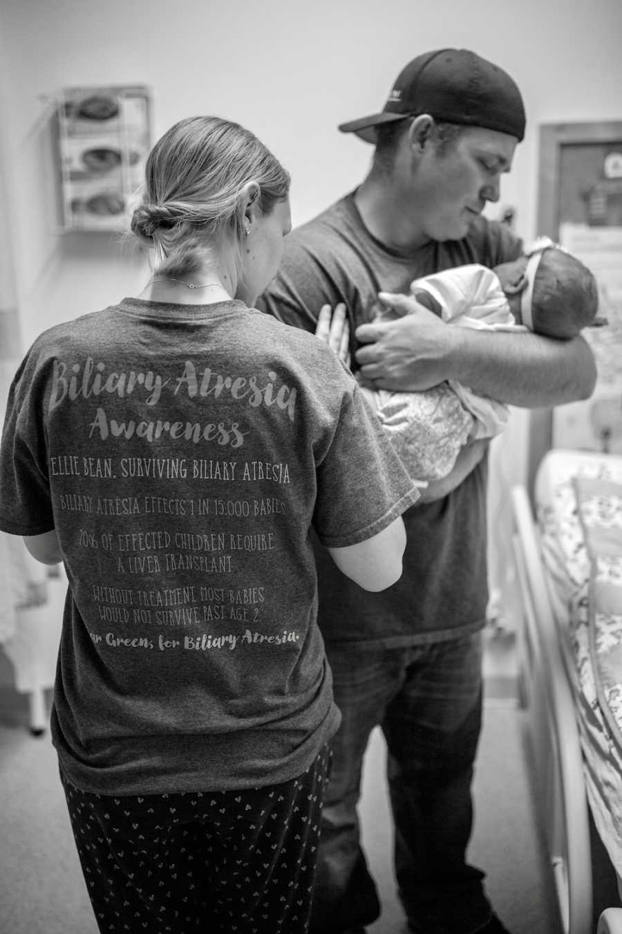 Mother wearing Biliary Atresia t-shirt stands beside husband as he holds baby daughter