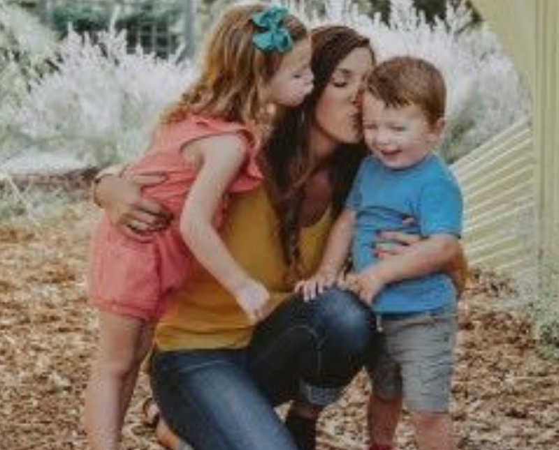 Woman who was abused kneels on ground kissing her son while her daughter kisses her