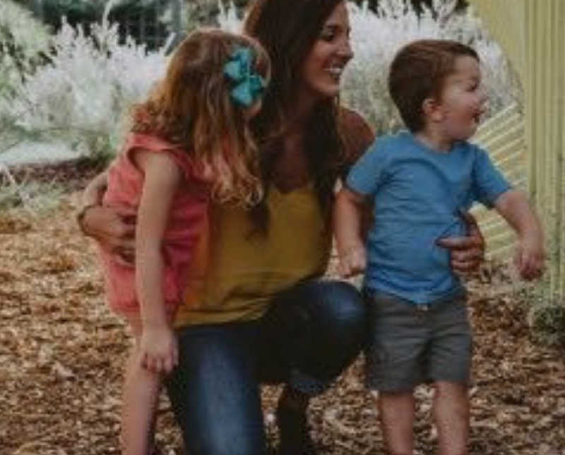 Woman who used to be abused smiles as she kneels beside her two young kids